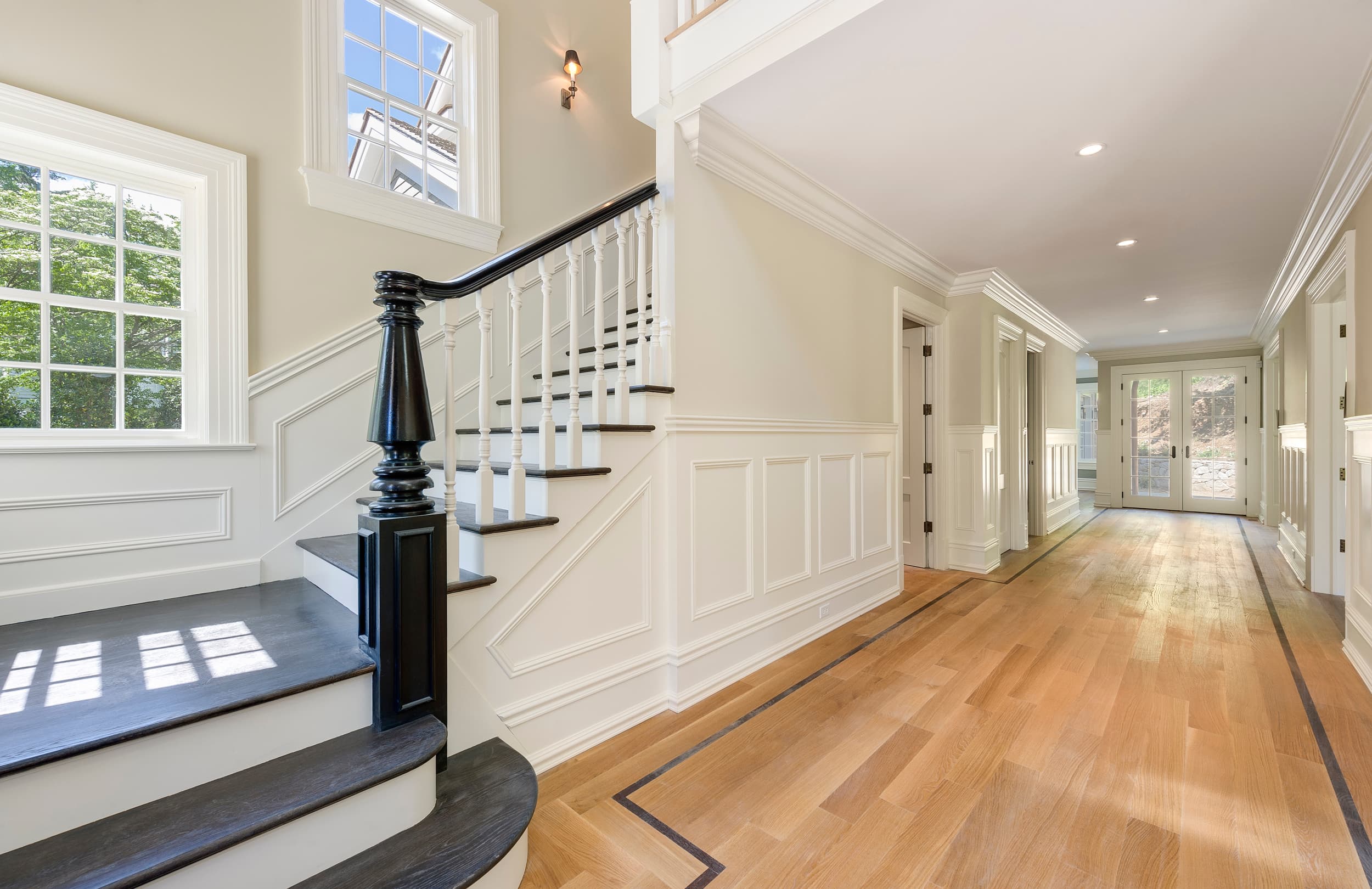 The foyer of the Dearfield residence: a timber stair with a carved newel post above an inlaid floor